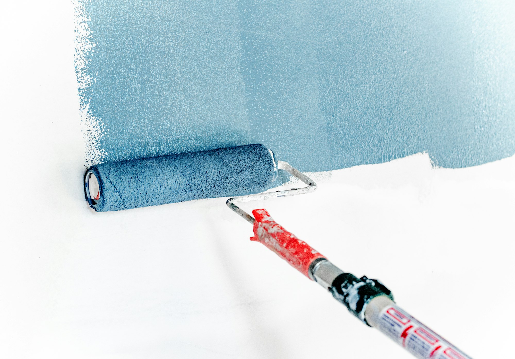 Rodillo aplicando pintura azul sobre una pared blanca